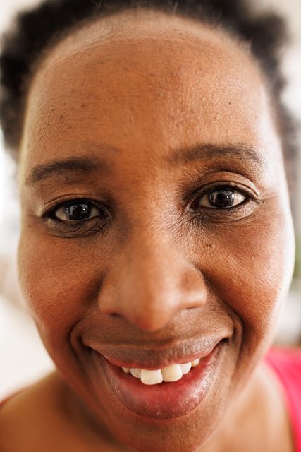 This image captures a close-up portrait of a smiling African American senior woman at home. It can be used in articles and advertisements related to senior lifestyle, happiness, aging gracefully, and domestic life. It is also suitable for use in healthcare, wellness, and family-oriented content.