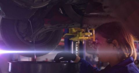 Mechanic Monitoring Oil Drainage under Lifted Car in Workshop