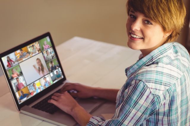 Woman using a laptop for an online video conference, engaging with multiple people in a grid view. She is smiling, suggesting a positive and friendly interaction. This can be used for illustrating concepts related to remote work, online education, digital communication, and modern technology in daily life.