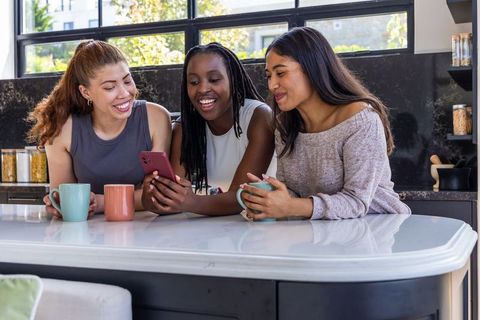 Friends sharing coffee and scrolling phone at modern kitchen island in sunlight