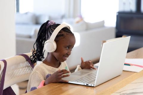 Smiling african american girl studying on laptop with headphones at modern home counter