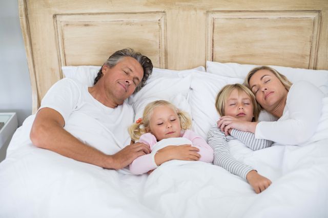 Family sleeping peacefully in bed together, showcasing a loving and cozy moment. Ideal for use in articles or advertisements related to family life, parenting, sleep health, and home comfort. Perfect for illustrating concepts of family bonding, relaxation, and restful sleep.