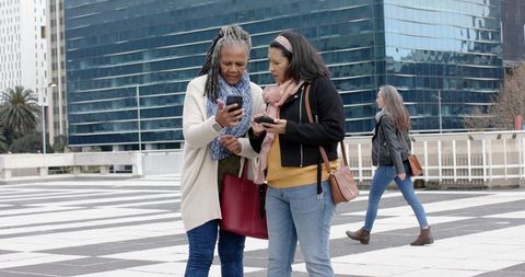 African American senior woman and friend comparing smartphones on downtown plaza
