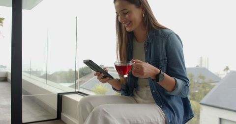 Woman Relaxing with Tea and Smartphone on Modern Balcony