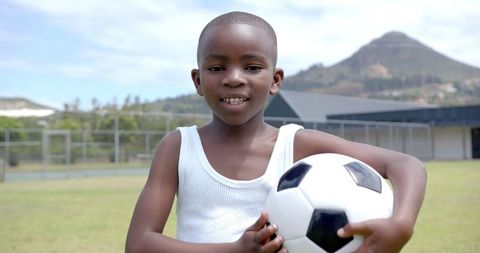 Smiling Child Holds Soccer Ball on Outdoor Field