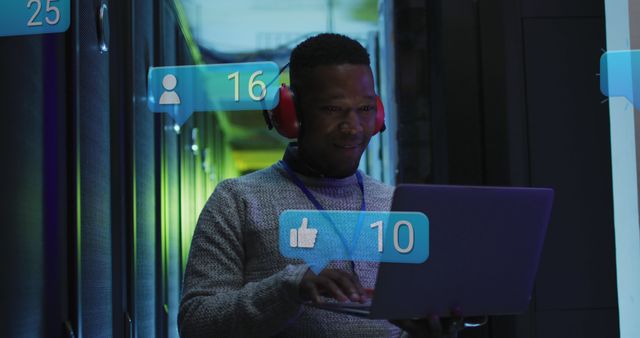Image of social media icons over african american male engineer using laptop at server room. Social media networking and business data storage technology concept