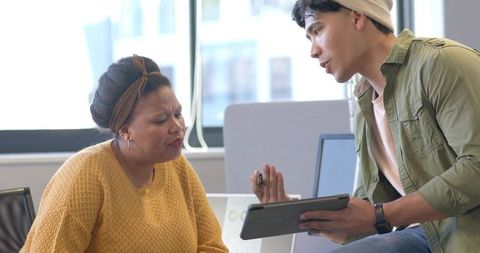 Collaborating over tablet in sunlit modern office, coworker coaching and discussing ideas