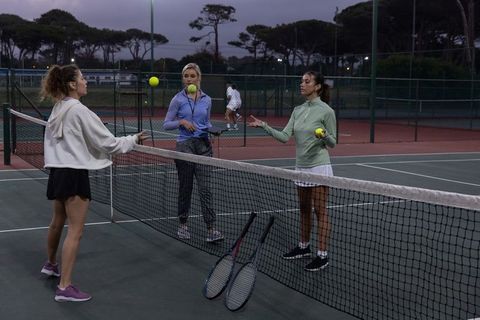 Twilight tennis practice three women training on outdoor courts with rackets and balls