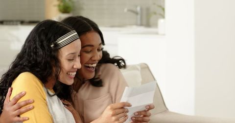 Two Women Reading Letter on Couch, Sharing Joyful Moment