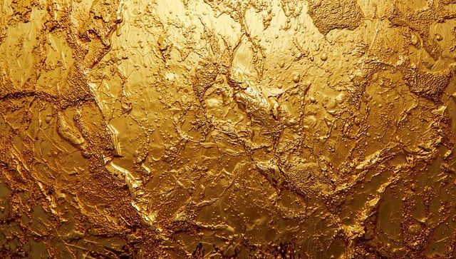 Textured metallic gold surface with ridges and droplets