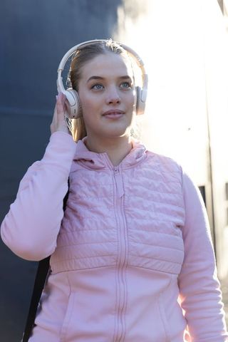 Young woman listening to music with over-ear headphones wearing pink quilted jacket urban