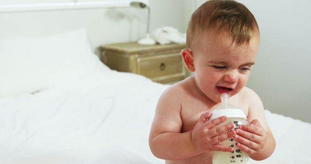 Irritated Baby with Feeding Bottle in White Bedroom - Download Free Stock Images Pikwizard.com