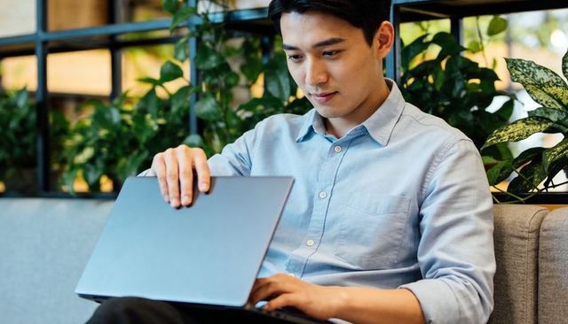 Young man typing on laptop while holding lid in biophilic coworking cafe with greenery