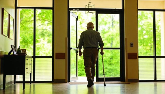 Senior man walking with cane through glass doors toward nature view conveying independence