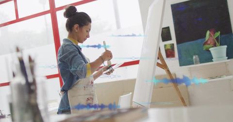 Female artist painting on canvas mixing colors on palette in bright sunlit studio