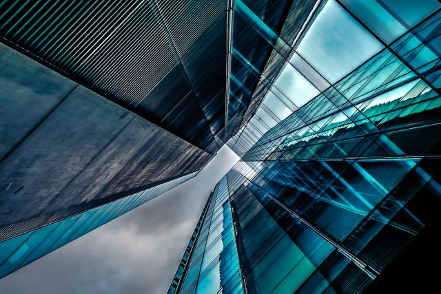 This stock photo captures a stunning upward perspective of modern glass skyscrapers with unique reflective angles against a cloudy sky. The clean lines and vibrant reflections highlight contemporary urban architecture, evoking themes of progress, innovation, and corporate environments. Ideal for use in business presentations, real estate advertisements, architectural portfolios, and urban planning magazines.