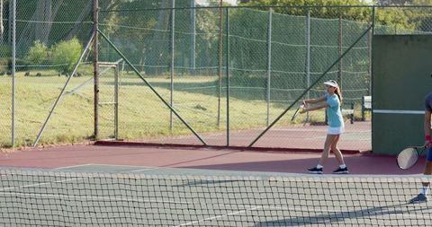 Mixed doubles players preparing backhand on outdoor tennis court baseline wearing visors