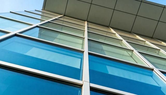Upward perspective of blue glass facade with grid mullions and roof canopy