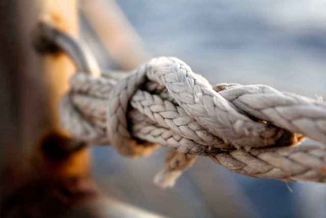 Zoomed-in view of a sturdy knot on a weathered nautical rope, suitable for illustrating themes of strength, durability, and seamanship. Ideal for use in articles, advertisements, or educational materials related to boating, marine equipment, and sailing practices.