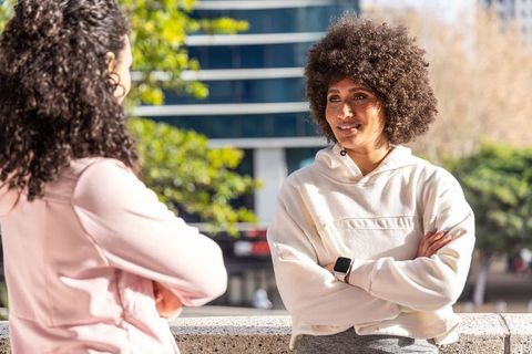 Two friends chatting on city plaza ledge, wearing hoodies and smartwatch, urban lifestyle