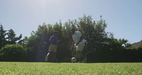 Father and son playing soccer on sunny backyard lawn, african american family lifestyle