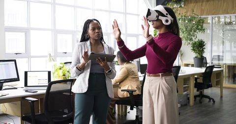 Female coworkers testing virtual reality headset in open office for team collaboration