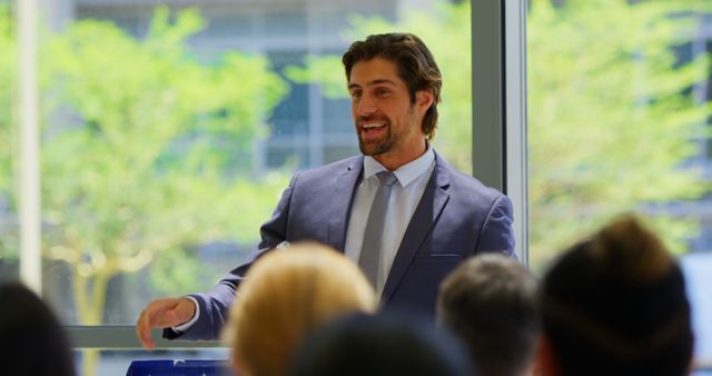 Smiling businessman delivering a presentation in a bright, modern office. Ideal for content related to business meetings, corporate training, professional settings, public speaking, and leadership roles.