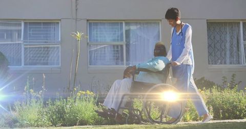 Nurse Assisting Senior Man in Wheelchair on Sunny Day Outdoors