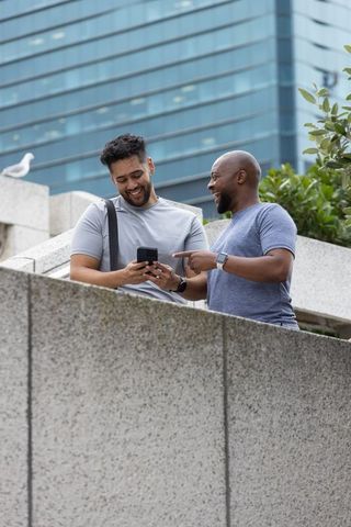 Two african american men laughing and pointing at smartphone on urban terrace in downtown