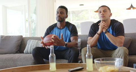 Friends watching football at home holding ball and snacks during tense game moment