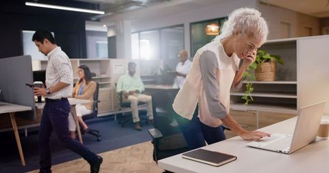 Senior businesswoman multitasking on laptop and phone in modern office