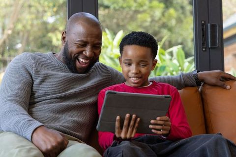 African american father and son laughing together while sharing tablet on couch