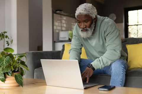 Senior african american man leaning forward typing on laptop in cozy home living room