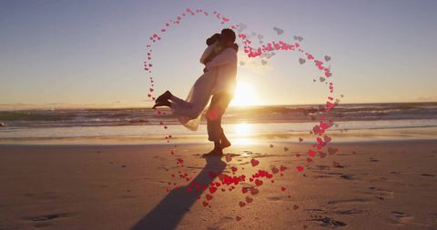 Joyful newlywed couple dancing on beach at sunset