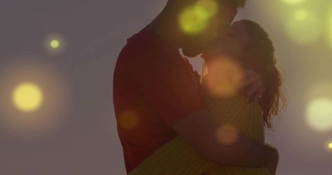 Couple kissing at sunset with warm lens flare and golden bokeh for romantic storytelling