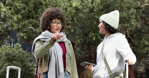 Diverse female friends chatting with luggage and phone, wearing scarves and beanie