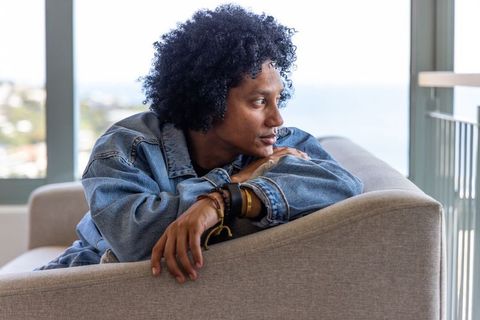 Contemplative african american man reclining on sofa in denim jacket looking out ocean view