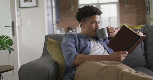 Young Man Relaxing at Home Drinking Coffee and Reading Book - Download Free Stock Images Pikwizard.com