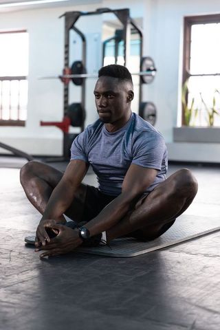 African american athlete stretching on mat in gym practicing butterfly stretch