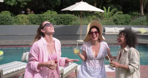 Diverse friends laughing poolside enjoying cocktails and sunshine in backyard