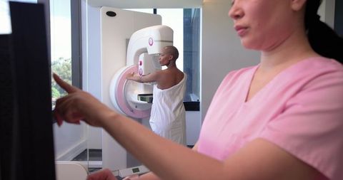 Diverse Female Patient Receiving Mammogram While Technician Operating Console in Clinic