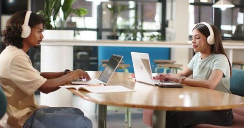 Young adults collaborating and working remotely at bright coworking table with headphones