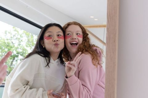 Diverse friends posing with under-eye patches wearing hoodies taking playful mirror selfie