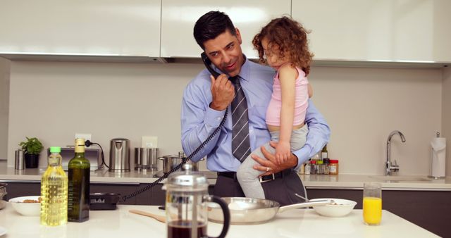 Smiling father holding his young daughter talking on the phone at home in the kitchen