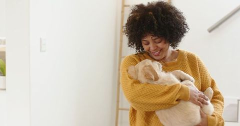 African american woman holding golden retriever puppy while smiling in cozy modern home