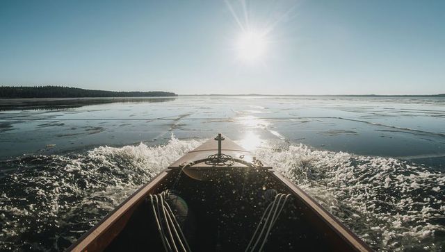 Wooden boat bow breaking thin lake ice at sunrise with ropes and cleat, winter navigation