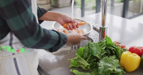 Woman Washing Carrots in Colander at Modern Stainless Kitchen Sink with Fresh Produce