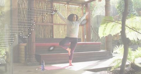 Practicing tree pose on wooden deck under pergola, balancing yoga in garden sunlight