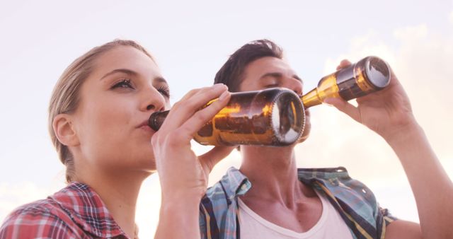 Young adults enjoying bottles of beer together outdoors. Ideal for concepts related to leisure, relaxation, outdoor gatherings, social scenes, and summer activities. Useful for promoting alcoholic beverages, lifestyle blogs, social event advertisements, and community gathering highlights.