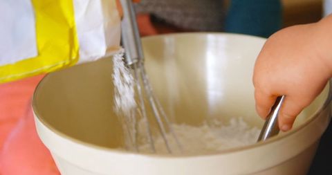 Close-up of parent and child baking together, mixing flour in bowl